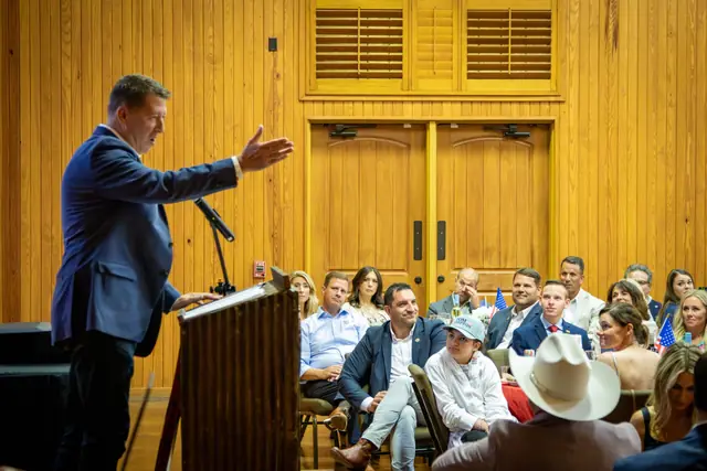 A speaker addressing a seated audience from the podium at a party event