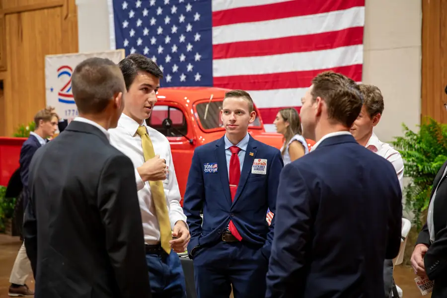 Younger attendees in suits talking together beside a vintage truck at the Legacy of Liberty dinner
